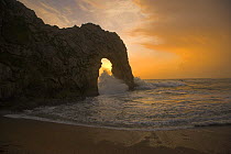 Sun setting and waves crashing through the arch at Durdle Door, Dorset, UK