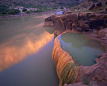 Cliffs, glowing orange from the sunrise, reflect in the Colorado River beside Pumpkin Spring's tavertine bowl in Grand Canyon National Park, Arizona
