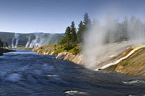Excelsior Geyser spilling over 4000 gallons per minute of boiling water into the Firehole River (far right), Midway Geyser Basin, Yellowstone National Park, Wyoming, USA (It is considered to be the la...