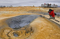 Person photographing bubbling hot mud springs, geothermal area of Krafla, North Iceland