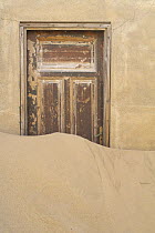 Door with sand covering the bottom of it, Kolmanskop, a deserted diamond mining town, Namib desert, Namibia.