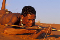 Bushman San lying on sand dune with traditional bow, Kalahari desert, Botswana