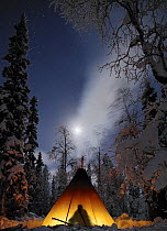 Man silhouetted inside Tepee with light, full moon, Lapland, Finland, January 2006