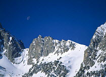 Moon above snow-covered rocky peaks in d'Aiguestortes National Park, Pallars Sobira, Catalonia, Spanish Pyrenees