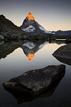 Sun hitting the peak of The Matterhorn (4478m) at sunrise with reflection in Lake Riffelsee, Switzerland