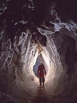 Potholer wallking along narrow underground passage, Cova Lachambre, Ria, Conflent, Pyrenees, France
