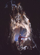 Potholer emerges from underground passage into cave with stalactites, Cova Lachambre, Ria, Conflent, Pyrenees, France