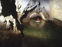 Potholer travelling through flooded underground passageways in small inflatable boat, Cueva Cuvera, Lago de Entrada, Ason, Cantabria, Spain