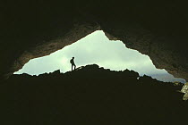 Potholer silhouetted at exit to underground cave system, Huesco, Spain