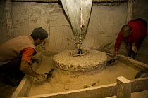 Two men grinding  barley with traditional mill stone at watermill, Dargye, Sichuan Province, Tibet, China