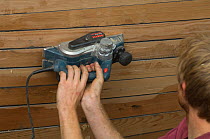 Shipwright planing carvel planked hull of Bristol Channel Pilot Cutter "Morwenna" with an electric sander. RB Boatbuilding, Underfall Yard, Bristol Floating Harbour, England. July 2008, Model Released