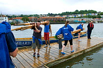 Mens and Ladies crews of Bristol Pilot Gig Club swapping oars, overlooked by Harbour Master. Their gig "Isambard" moored alongside pontoon at Bristol's Floating Harbour, England, UK. July 2008