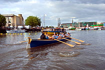 Bristol Pilot Gig Club's Ladies crew practicing in their gig "Isambard" on Bristol Floating Harbour, with city skyline and Bristol Ferry in background. England, UK. July 2008, Model Released