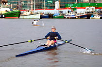 Woman sculling and man kayaking on Bristol Floating Harbour, with boats moored in background, UK, July 2008