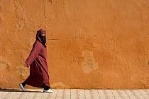 Muslim woman walks past wall, Medina del Zoco, Marrakech, Morocco