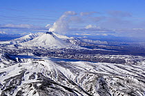First snow on the smoking Karymsky volcano and lake in October, Kronotsky Zapovednik, Kamchatka, Far East Russia.