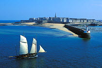 Bisquine classic yacht ailing past long pier of Saint Malo, Brittany, France