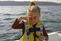 Little girl shielding eyes from the sun, and helming small boat. Brest, France 2002