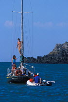 Two people in Honda marine inflatable approaching yacht, with man standing on mast, 2004