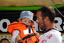 Crew member Damian Foxhall holding child in lifejacket, after finishing leg one of the 10th Volvo Ocean Race in fourth position in "Green Dragon". Cape Town, November 2008. For EDITORIAL USE only.