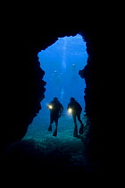 Divers with torches silhouetted at the entrance to First Cathedral cave off the Island of Lanai, Hawaii. August 2007. Model released