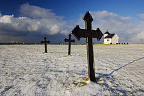 Snow covers the ground of the old churchyard of Varhaug, Hå, Rogaland, Norway. Note World War II bullet hole in Iron cross. February