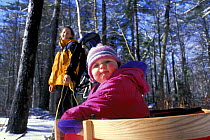 A young girl (age 2) is pulled in a toboggan by her mother at the Rachel Carson National Wildlife Refuge, Kennebunk, Maine, USA.