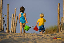 A young sister and brother (ages 2 and 4) on their way to play on the beach at the Cape Cod National Seashore in Truro, Massachusetts, USA