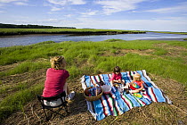 Family enjoying a picnic next to a tidal estuary on Plum Island Sound, Massachusetts, USA