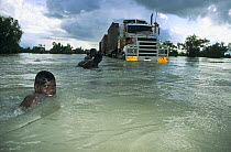 Aborigine children playing in flooded river beside stranded vehicle, Queensland, Australia