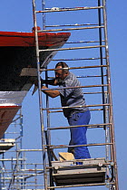 Man on scaffolding repairing a boat at Le Guilvinec, Finistere, Brittany, France 1999.