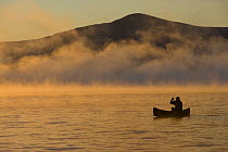 Canoeing in Lily Bay iin the mist at sunrise, Moosehead Lake, Maine, USA. Lily Bay Mountian is in the distance. model released