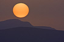 Large orange sun setting over mountains, Southern Morocco, NW Africa