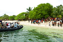 Tourists arrive by zodiac boat and are greeted by locals at Bodaluna Island, Woodlark / Laughlan Islands, Papua New Guinea. (Also known as Budi Budi Island) May 2008