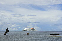 Local canoes in bay with Clipper Odyssey tourist cruise boat moored off Nembao Village, Utupua Island, Solomon Islands