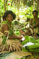 Young women in traditional dress preparing meal for tourist demonstration, Rano Island, Vanuatu May 2008