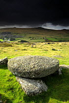 Hut circle remains and large circular granite slab, against stormy sky, Merrivale, Dartmoor NP, Devon, UK. September 2008.