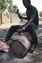 Gambian man using hammer and chisel to break apart old gas canister, The Gambia, 2008