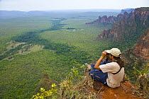 Man looking through binoculars at landscape from top of cliff, Chapada dos Guimares NP, Chapada, Mato Grosso, Brazil