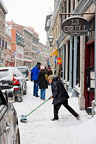 Man shovelling snow on pavement outside shop. Montreal, Canada, 2008.