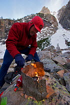 Phil Atkinson starting stove at his camp site in the Box Canyon along East Rosebud Creek, Bearthooth Mountains, Montana, USA.  May 2008