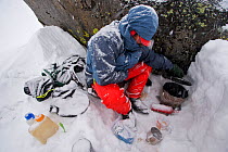 Skier Phil Atkinson cooks dinner in a snow storm at a camp near Sky Top Lakes, on the approach to Granite Peak, Beartooth Mountains, Montana, USA. May 2008