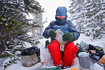 Phil Atkinson preparing dinner during a snow storm at a camp near Denny Lake, Beartooth Mountains, Montana, USA. May 2008