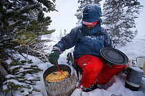 Phil Atkinson preparing dinner during a snow storm at a camp near Denny Lake, Beartooth Mountains, Montana, USA. May 2008