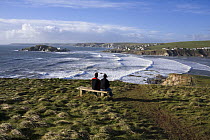 Couple sitting on bench on coastal path near Bantham Bay, with Burgh Island in the distance. South Devon, UK. January 2009.