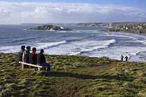Friends sitting on bench on coastal path near Bantham Bay, with Burgh Island in the distance. South Devon, UK. January 2009.