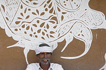 Rajasthani man beside traditional painting on mud wall of house during Diwali festival, Bada Gaire Killa village, Rajasthan, India