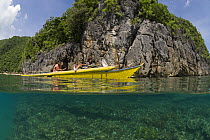 Family in their outrigger boat, split-level showing coral reef and limestone cliffs in the Caramoan Peninsula, Camarines Sur, Luzon, Philippines