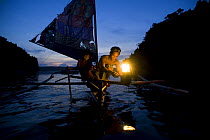 Fisherman and son on traditional sailboat out for night fishing using a kerosine ^Petromax^ lamp to attract fish, Camarines Sur, Luzon, Philippines 2008.