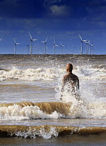 A sculpture of a person in the sea with an offshore windfarm in the distance, Anthony Gormley sculpture Another Place, Crosby, Liverpool, UK, October 2008